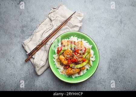 Asiatisches süß-saures Hähnchen mit Gemüse, gebraten und Reis in einer Keramikschale mit Stäbchen von oben, grauer rustikaler ston Stockfoto