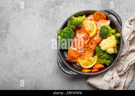 Gesunder gebackener Fisch Lachssteaks, Brokkoli, Blumenkohl, Karotte in schwarzer gusseiserner Auflaufschale auf grauem Steinhintergrund. Kochen Stockfoto