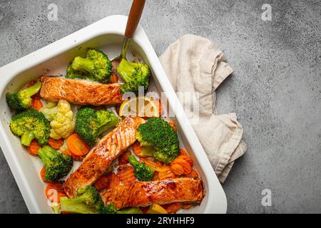 Blick von oben auf gesunde gebackene Fisch Lachssteaks, Brokkoli, Blumenkohl, Karotte in Auflaufform auf grauem Steinhintergrund. Kochen Stockfoto