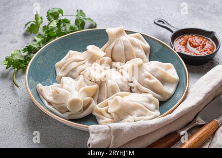 Georgianische Khinkali-Knödel auf Teller mit roter Tomatensauce und frischem Koriander-Winkel, rustikaler Steinhintergrund, traditionelles d Stockfoto