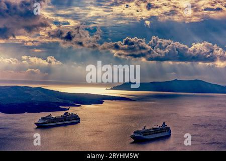 Hafen von Santorin in goldenem Licht mit vor Anker liegenden Kreuzfahrtschiffen Stockfoto