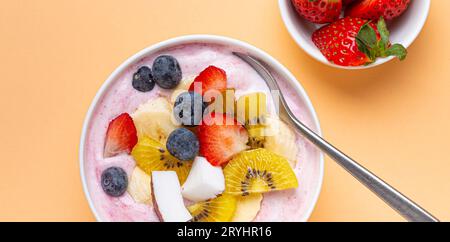 Gesunde Frühstücks- oder Dessert-Joghurtschale mit frischer Banane, Erdbeere, Heidelbeere, kokos, Kiwi-Draufsicht auf minimalem Pastellpapier Stockfoto