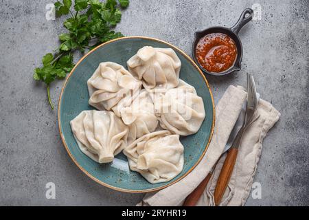 Georgianische Khinkali-Knödel auf Teller mit roter Tomatensauce und frischem Koriander von oben, rustikaler Steinhintergrund, traditionelles Dessert Stockfoto