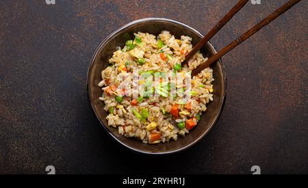 Authentischer chinesischer und asiatischer gebratener Reis mit Ei und Gemüse in brauner Keramikschale mit Blick von oben, dunkler rustikaler Betontisch Backgr Stockfoto