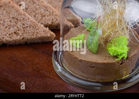 Reichhaltige und cremige Leberpastete mit Kräutern und getoastetem Brot unter einer Glaskuppel Stockfoto