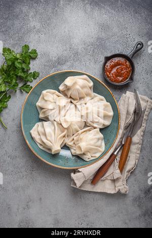 Georgianische Khinkali-Knödel auf Teller mit roter Tomatensauce und frischem Koriander von oben, rustikaler Steinhintergrund, traditionelles Dessert Stockfoto