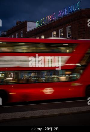 Brixton, London, Großbritannien: Ein roter Londoner Bus mit Bewegungsunschärfe, der nachts entlang der Brixton Road fährt. An der Kreuzung mit Electric Avenue mit Neonschild. Stockfoto