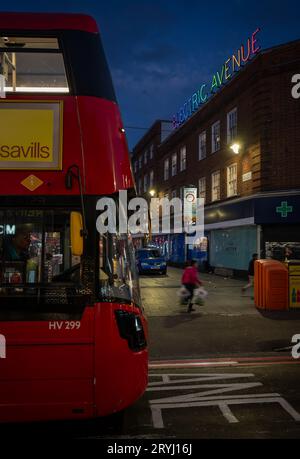 Brixton, London, Großbritannien: Ein roter Londoner Bus fährt nachts entlang der Brixton Road. An der Kreuzung mit der Electric Avenue und ihrem farbenfrohen Neonschild. Stockfoto