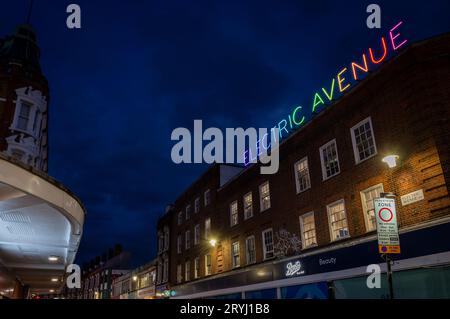Brixton, London, Großbritannien: Electric Avenue in Brixton bei Nacht. Von der Brixton Road mit dem farbenfrohen Neonschild Electric Avenue aus gesehen. Stockfoto