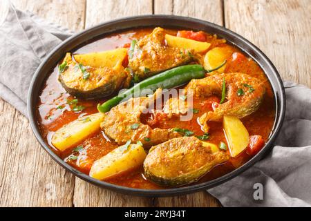 Machher Jhol oder Machha Jhola, ist ein traditionelles, würziges Fischcurry in Bengali und Odia Küche, das auf dem Holztisch auf dem Teller steht. Horizontal Stockfoto