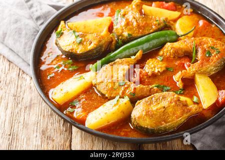 Authentisches bengalisches Fischcurry mit Kartoffelcloseup auf dem Teller auf dem Holztisch. Horizontal Stockfoto