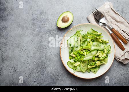 Gesunde vegane grüne Avocado Salatschüssel mit geschnittenen Gurken, Edamame Bohnen, Olivenöl und Kräutern auf Keramikplatte Draufsicht, grau Stockfoto