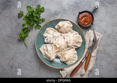 Georgianische Khinkali-Knödel auf Teller mit roter Tomatensauce und frischem Koriander von oben, rustikaler Steinhintergrund, traditionelles Dessert Stockfoto