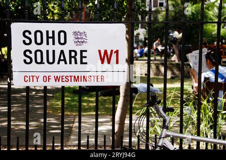 Soho Square W1 weißes Westminster-Schild mit Park im Hintergrund und Person, die Zeitung in der Sonne liest Stockfoto