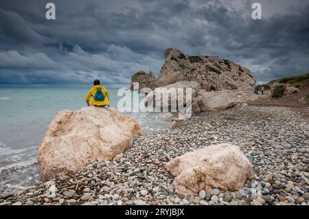 Frau sitzt auf einem Felsen und genießt die Meereslandschaft im Winter. Stürmische Wolken am Strand Stockfoto