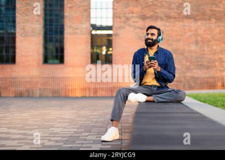 Ein Mann Aus Dem Nahen Osten Mit Smartphone Und Kopfhörern, Der Musik Im Freien Genießt Stockfoto