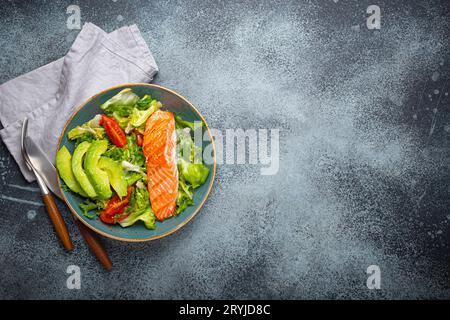 Gegrilltes Fisch Lachssteak und Gemüsesalat mit Avocado auf Keramikplatte auf rustikalem Steinhintergrund Draufsicht, ausgewogene Ernährung, Stockfoto
