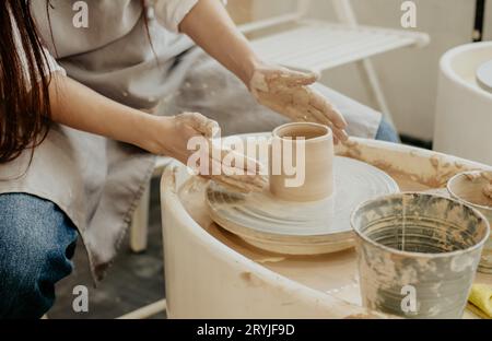 Frauen modellieren einen Tontopf auf einem Töpferrad aus einem speziellen Holzwerkzeug. Kreativer Workshop. Die Frauen modellieren aus Lehm. Arbeitsatmosphäre im Haus Stockfoto