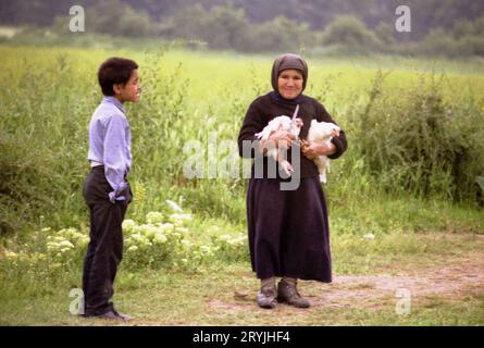 Ilfov County, Rumänien, 1990. Ältere Nonne, die zwei lebende Hühner und ein Messer hielt, das sie einem Dorfbewohner geben würde, um für ein Klostermahl zu opfern. Stockfoto