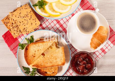 Geröstete Brotscheiben mit Käse und grüner Petersilie auf weißem Teller, Tasse Kaffee, Schüssel mit Strohhalm Stockfoto