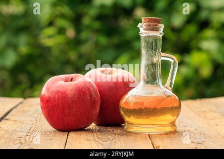 Apfelessig in Glasflasche und rote Äpfel auf Holzbrettern mit grünem natürlichem Hintergrund. Stockfoto