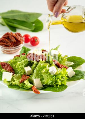 Salat aus sonnengetrockneten Tomaten, Käse und Salatblättern. Olivenöl gießt auf Salat Stockfoto