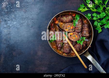 Traditionelle langsam gekochte deutsche Wagyu-Rindfleischrouladen mit Gemüse und Speck, serviert in scharfer Soße als Blick von oben in Kupfer Stockfoto