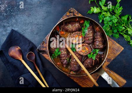 Traditionelle langsam gekochte deutsche Wagyu-Rindfleischrouladen mit Gemüse und Speck, serviert in scharfer Soße als Blick von oben in Kupfer Stockfoto