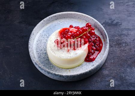 Traditioneller Vanillepudding, frische Johannisbeeren und Kompott, serviert als Nahaufnahme auf einem Teller im nordischen Design auf einem schwarzen Brett Stockfoto