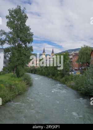 Der Fluss Rienza fließt durch die Stadt Bruneck und die Kirche im Hintergrund, Italien. Stockfoto