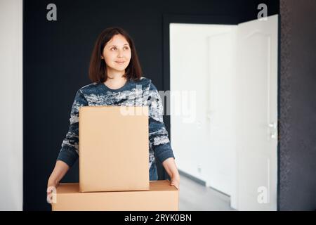 Junge lächelnde Frau zieht in eine neue Wohnung mit Pappkartons Stockfoto