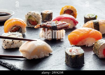 Sushi mit Stäbchen auf schwarzem Schiefergrund. Rollen, Maki, Nigiri Stockfoto