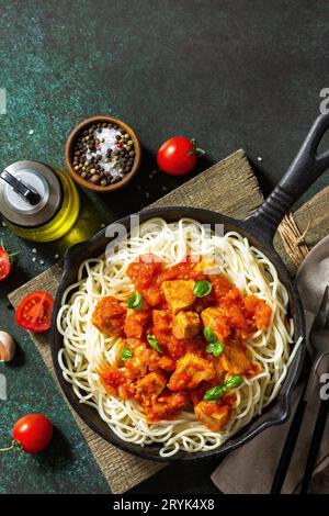 Gesundes Essen, italienische Pasta. Spaghetti mit Huhn und Gemüse in Tomatensauce in einer gusseisernen Pfanne auf einer Steinplatte. Stockfoto