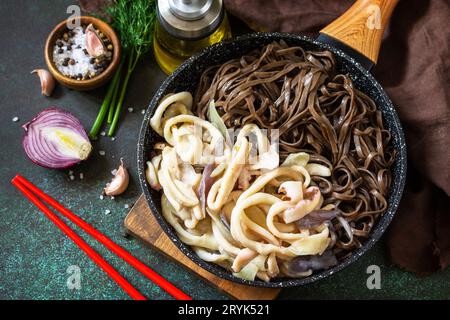 Würzige Nudeln, traditionelle koreanische Küche. Buchweizen-Soba-Nudeln und Tintenfisch mit saurer Sahnesauce auf einer Tischplatte aus dunklem Stein. Stockfoto