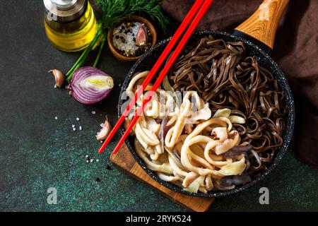 Würzige Nudeln, traditionelle koreanische Küche. Buchweizen-Soba-Nudeln und Tintenfisch mit saurer Sahnesauce auf einer Tischplatte aus dunklem Stein. Stockfoto