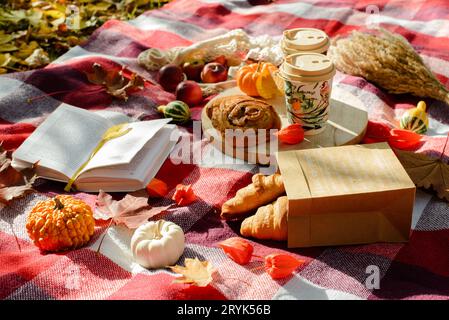 Picknick im Herbstwald. Bunte Blätter, Karos, Kaffee und Croissants, Kürbisse Stockfoto