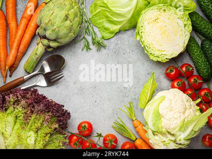 Frische Auswahl an Bio-Gemüse, Löffel, Gabel auf rustikalem grauem Steintisch, Kopierraum mit Blick von oben. Vegetarisches Essen Hintergrund und er Stockfoto