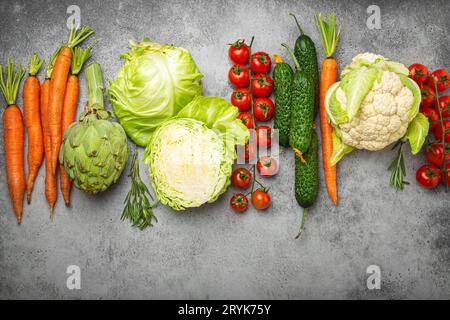 Frisches, gemischtes Bio-Gemüse in einer Reihe auf dem rustikalen grauen Steintisch mit Blick von oben angeordnet. Vegetarische Lebensmittel Hintergrund und gesund V Stockfoto