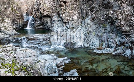 Wasserfall plätschert auf einem See und fließt durch den Fluss mit felsiger geologischer Formation. Stockfoto