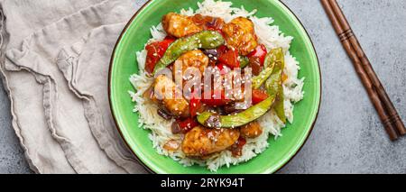 Asiatisches süß-saures Hähnchen mit Gemüse, gebraten und Reis in einer Keramikschale mit Stäbchen von oben, grauer rustikaler ston Stockfoto