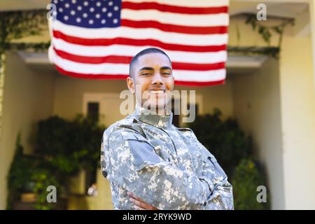 Porträt eines glücklichen, birassischen, männlichen amerikanischen Soldaten in Militäruniform, der vor dem Haus steht Stockfoto