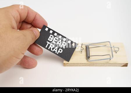 Ein Mann zieht den Köder aus einem Mousetrap. Köder, ein Blatt schwarzes Papier mit der Aufschrift - Bärenfalle. Finanz- und Rechtskonzept. Stockfoto