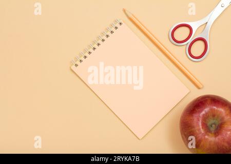 Schulbedarf. Ein Apfel, ein Notizbuch, ein Farbstift und eine Schere Stockfoto