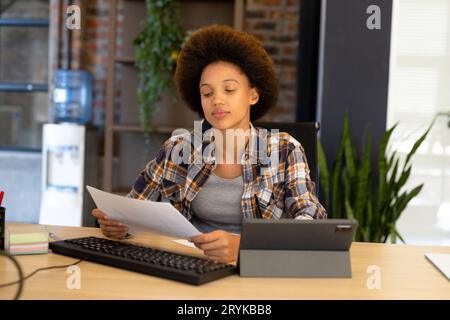Eine glückliche, birassistische Geschäftsfrau, die am Schreibtisch sitzt und Dokumente liest Stockfoto