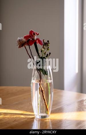 Ein Blumenstrauß in einer transparenten Vase auf einem Holztisch in den Sonnenstrahlen. Stockfoto