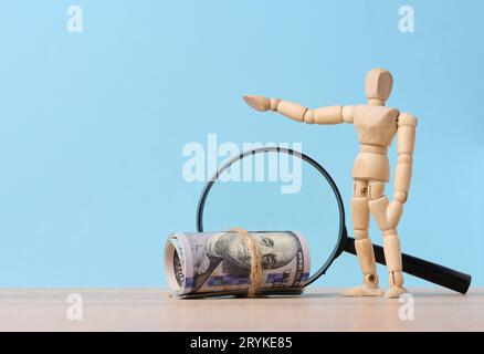 Hölzerne Schaufensterpuppe, Lupe und gebundenes Papier amerikanische Dollar auf blauem Hintergrund, das Konzept des Einkommenswachstums Stockfoto
