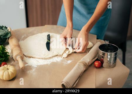 Nahaufnahme einer Frauenhände, die das Teigessen am Tisch in der Küche zubereiten. Pizza kochen Stockfoto