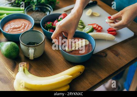 Weibliche Hände legen geschnittene Früchte auf eine Schüssel mit rosa Chia-Pudding. Hässliches Essen. Kochen gesunde leckere Speisen. Lifestyle. Stockfoto