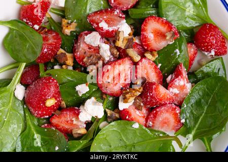 Nahaufnahme des leichten gesunden Sommersalats mit frischen Erdbeeren, Spinat, Rahmkäse und Walnüssen auf weißer Keramikplatte, weiß Stockfoto