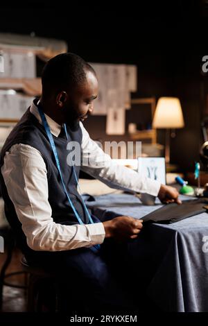 Lächelnder Couturier, der exquisite Business-Anzüge für die Kundenbetreuung zusammensetzt. Erfahrene Modedesignerin, die im Schneiderstudio arbeitet und stilvolle, maßgeschneiderte, sartoriale Kleidung kreiert Stockfoto